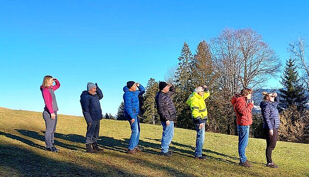 Sieben Menschen stehen auf einem Grasshügel hintereinander und schauen in die Ferne